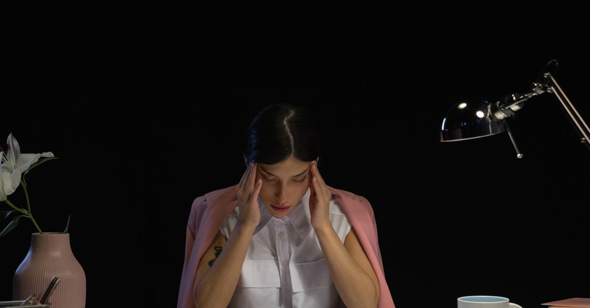 Woman sitting with her hands to her temples in low light