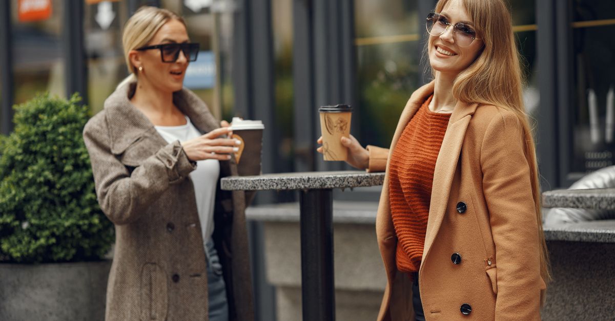 Two women in their forties talking outdoors with coffee