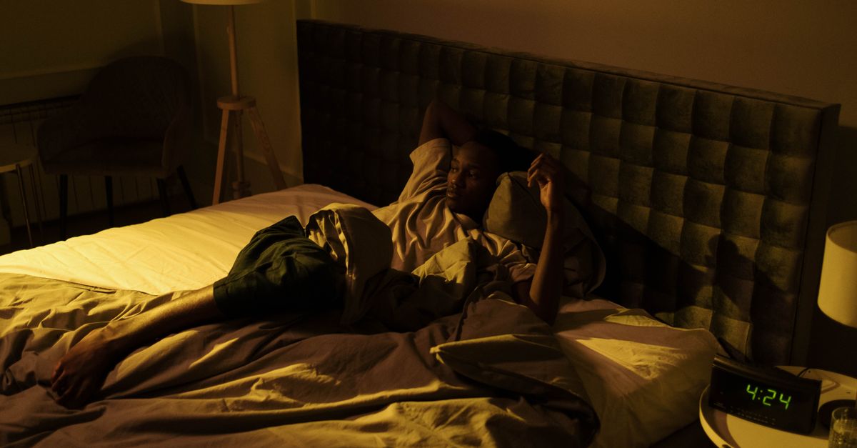 Woman lying awake in bed at night beside a clock reading 4:24