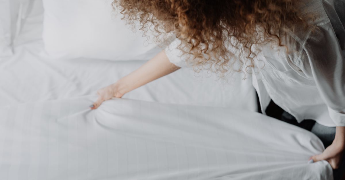 Woman smoothing a white sheet over a bed, the layered bedding that helps with cold night sweats
