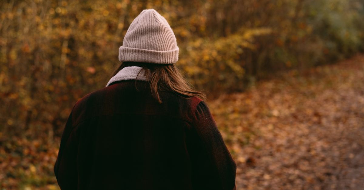 Woman in a warm hat walking a long autumn woodland path during perimenopause years