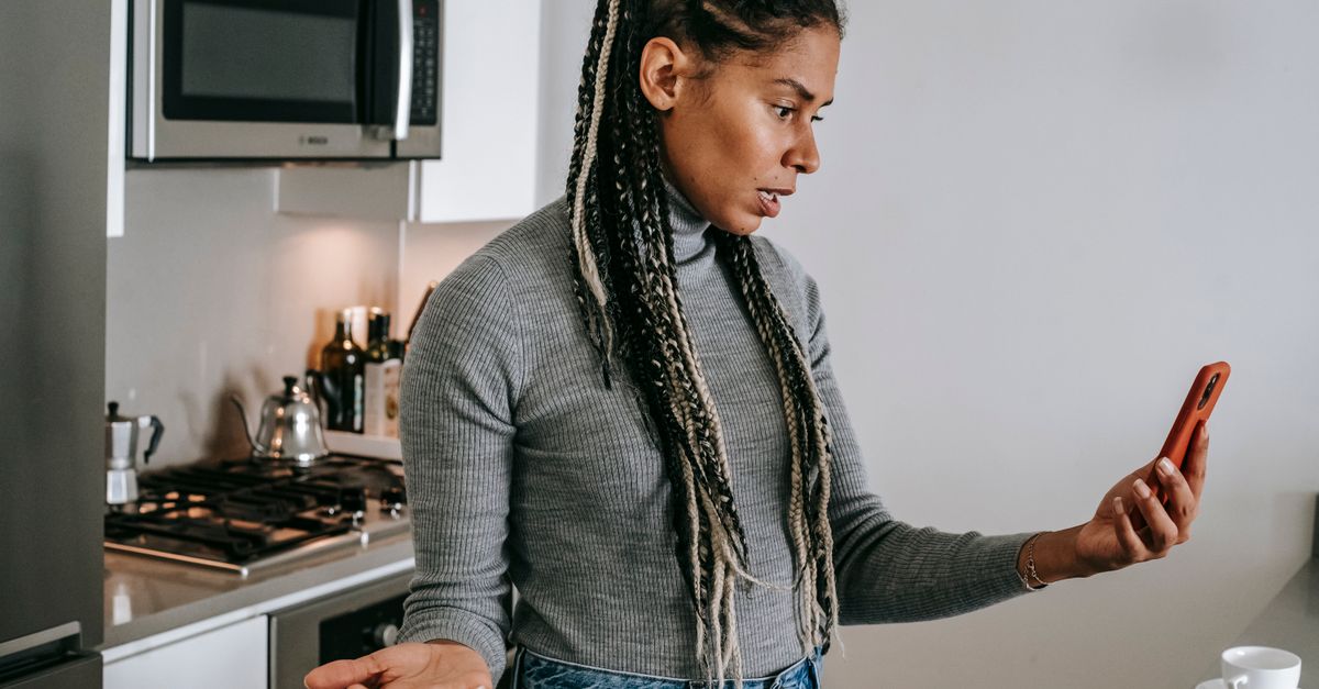 Woman in her forties in a kitchen looking exasperated at her phone