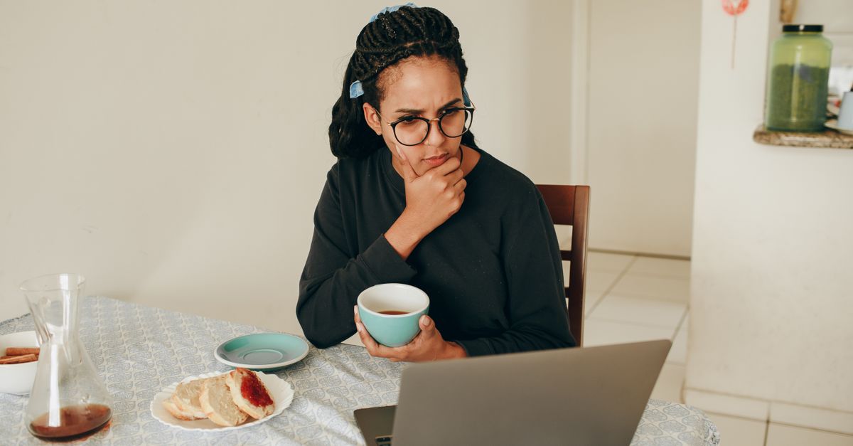 Woman in her forties at a kitchen table reading a laptop, searching what causes itchy skin in perimenopause