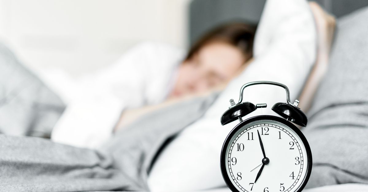Bedside alarm clock in focus while someone sleeps behind it, marking a perimenopause night waking