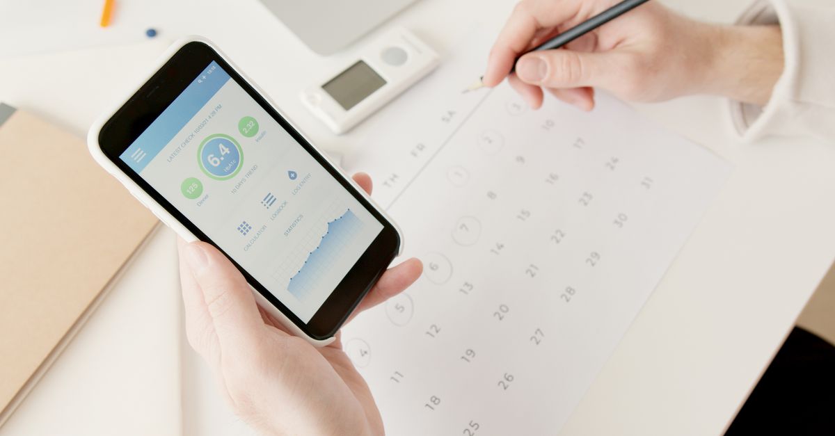 Hands holding a phone showing a health tracking app beside a paper calendar and pen