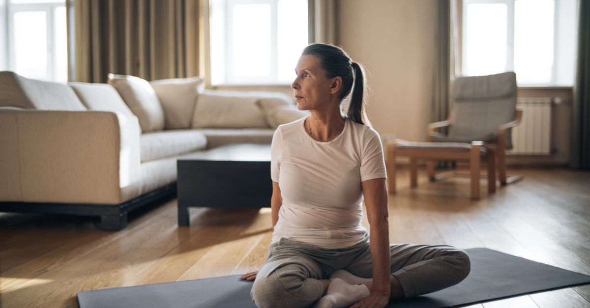 Woman sitting on a yoga mat in a living room, easing the joint stiffness of post menopausal symptoms